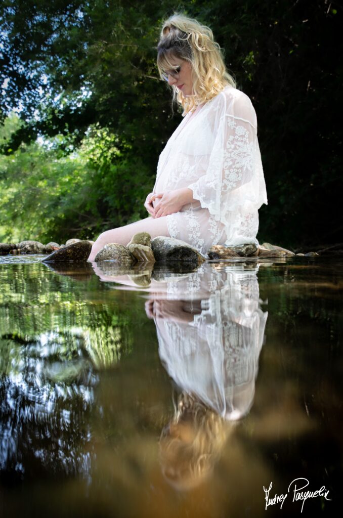 Phoo d'une femme enceinte entrain de tenir son ventre, assise au bord de l'eau